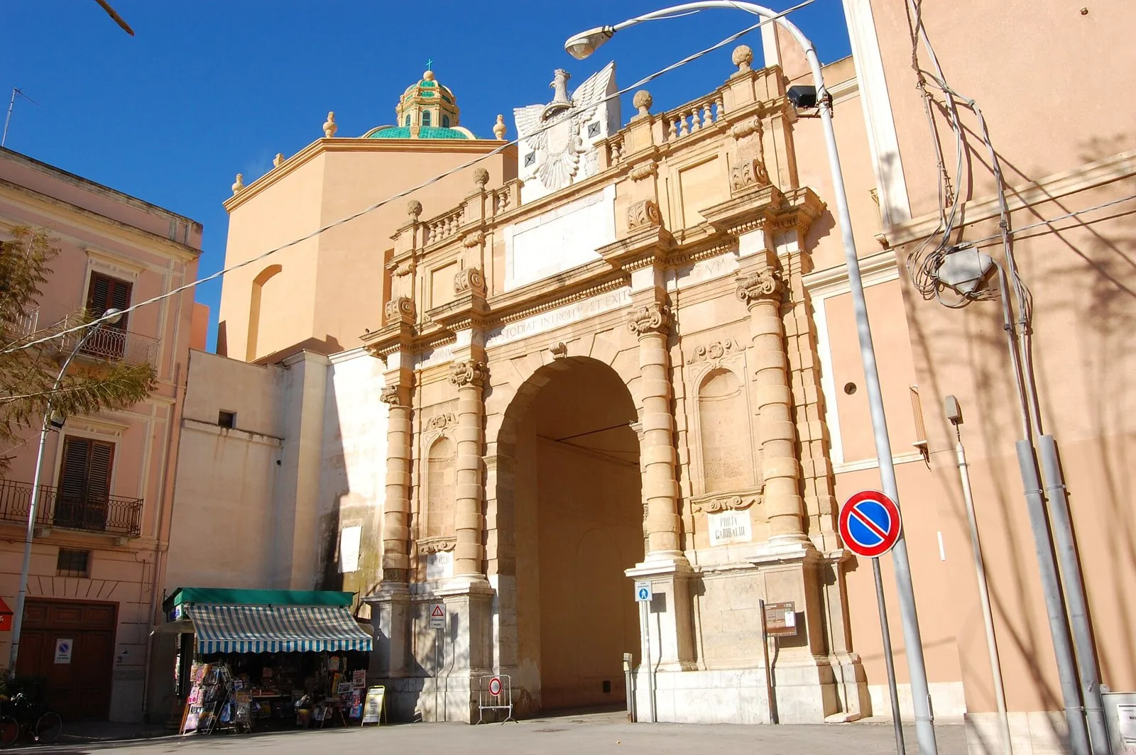 Porta Garibaldi a Marsala, arco barocco in pietra chiara con la cupola della chiesa dell'Addolorata sullo sfondo e cielo azzurro