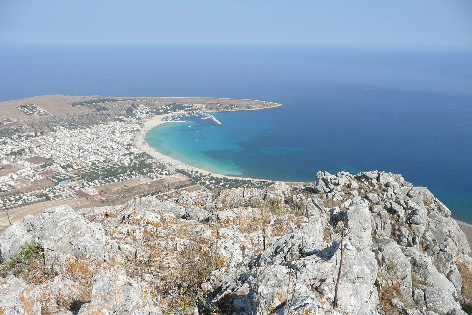 Veduta dall'alto della baia di San Vito Lo Capo, con la spiaggia chiara, il mare turchese, il paese e il faro sulla punta del capo