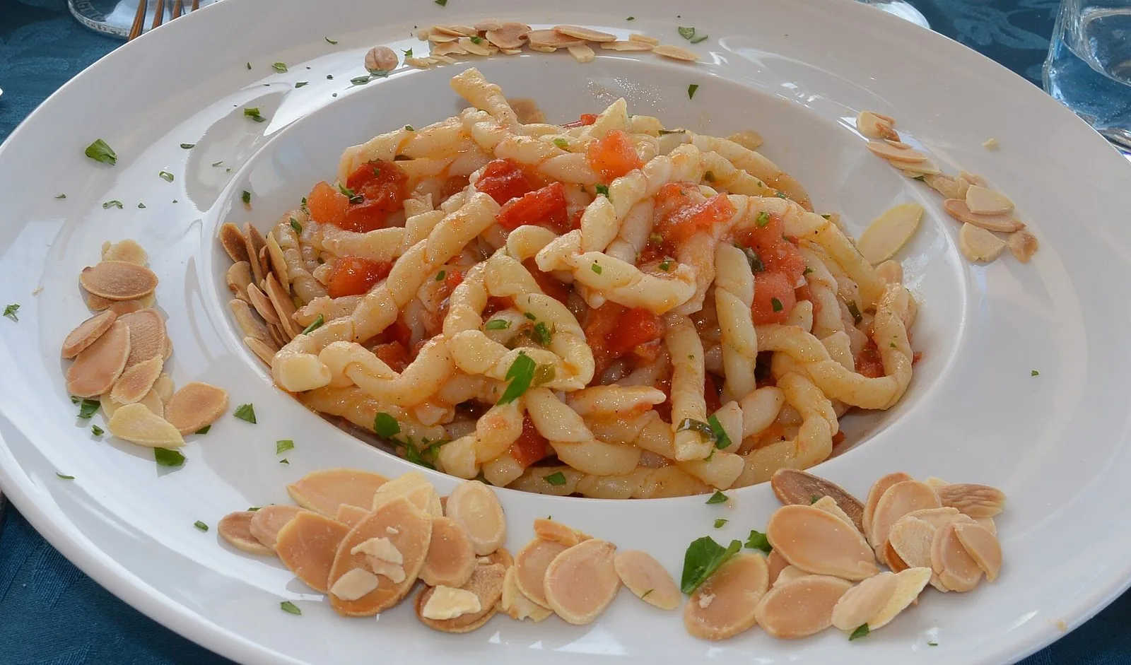 Piatto di busiate trapanesi con pomodoro fresco a cubetti, prezzemolo e mandorle a lamelle sul bordo