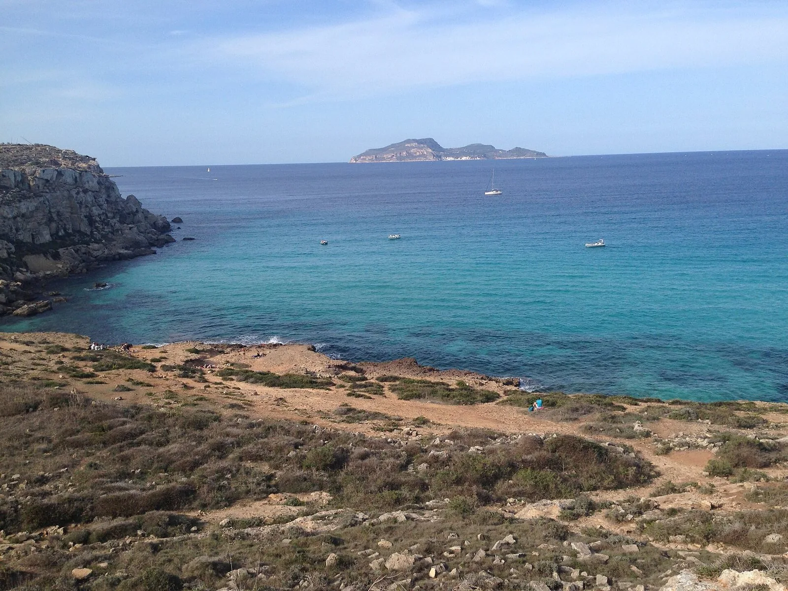 Cala Rossa a Favignana: mare turchese, costa rocciosa con macchia bassa e un'isola all'orizzonte