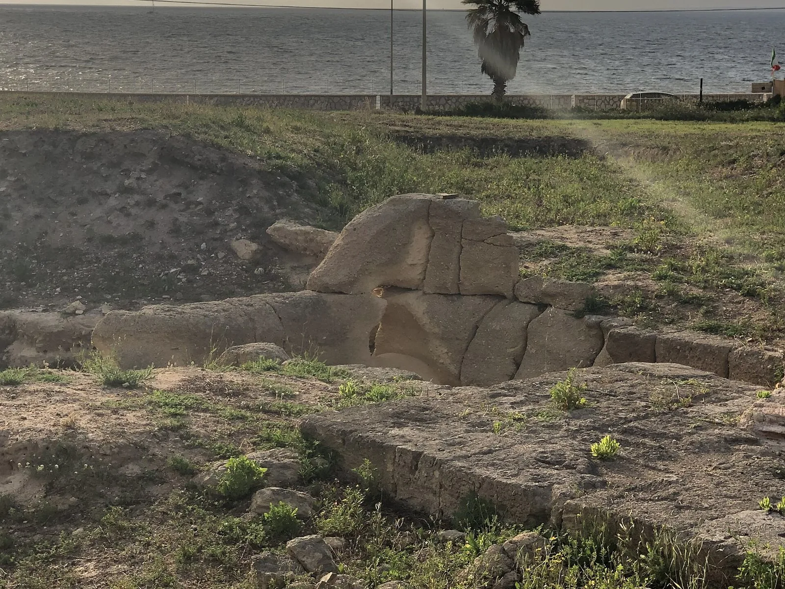 Resti di strutture antiche in blocchi di pietra tra l'erba nell'area archeologica di Lilibeo, con il mare sullo sfondo