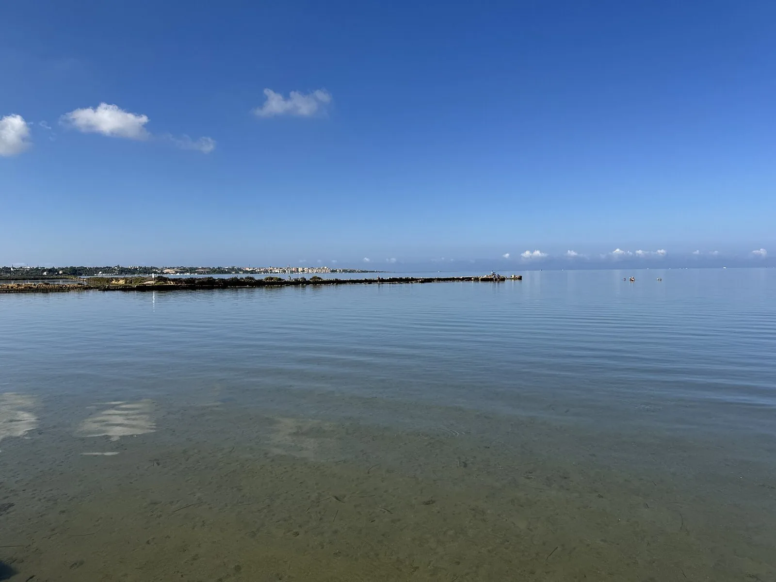 Mare calmo e trasparente dai fondali bassi sulla costa di Marsala, con la città all'orizzonte e cielo azzurro